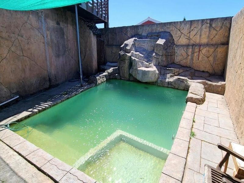 Outdoor pool area featuring a rock water feature, paved surround, and high boundary walls for privacy.