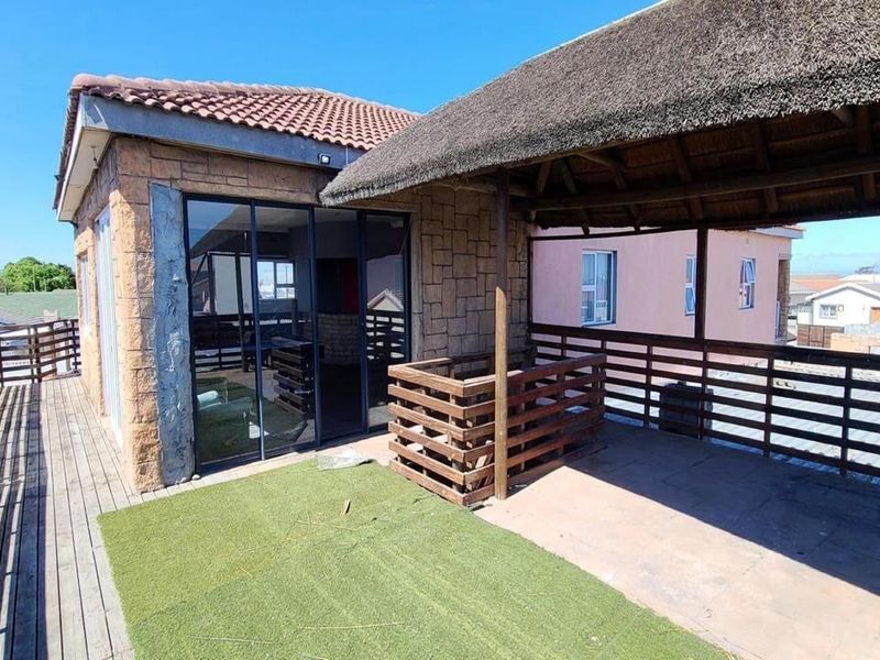 An elevated outdoor patio area featuring a thatched roof, timber decking, and stone-clad walls, offering a versatile space for outdoor relaxation.