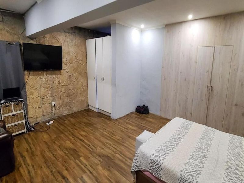 Spacious bedroom featuring laminate flooring, a textured stone feature wall, and ample built-in cupboard storage with recessed lighting.