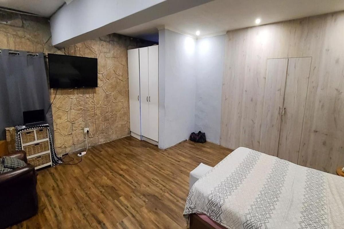 Spacious bedroom featuring laminate flooring, a textured stone feature wall, and ample built-in cupboard storage with recessed lighting.