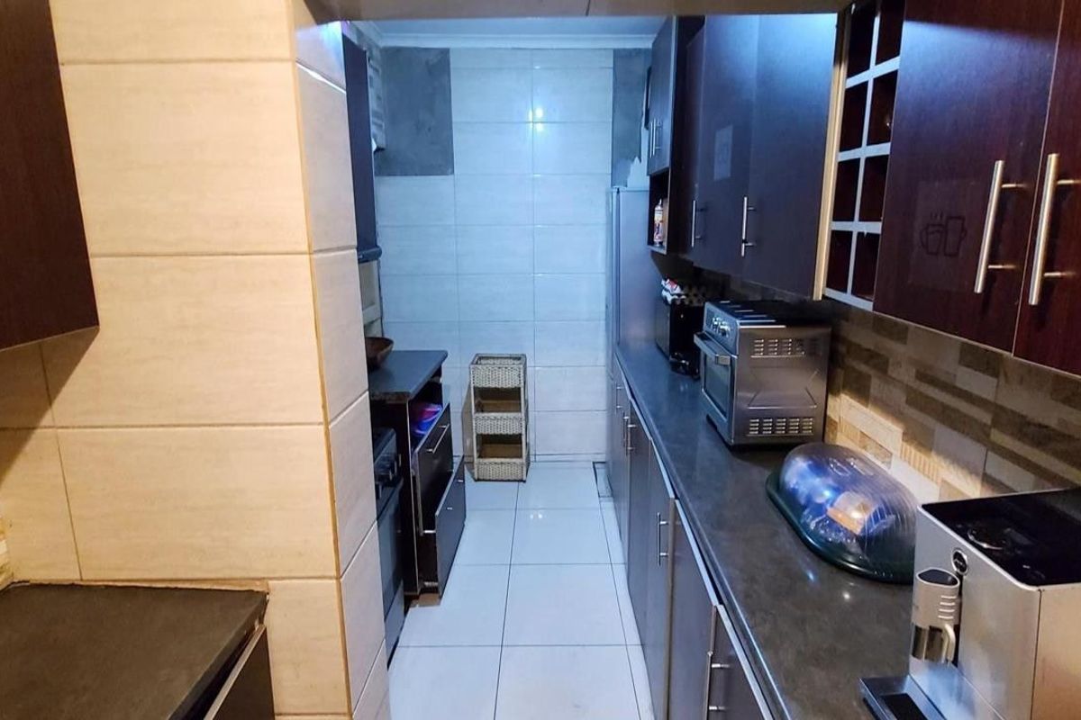 A galley-style kitchen featuring dark wood cabinetry, stone-look countertops, and tiled flooring, offering a functional layout with ample storage space.