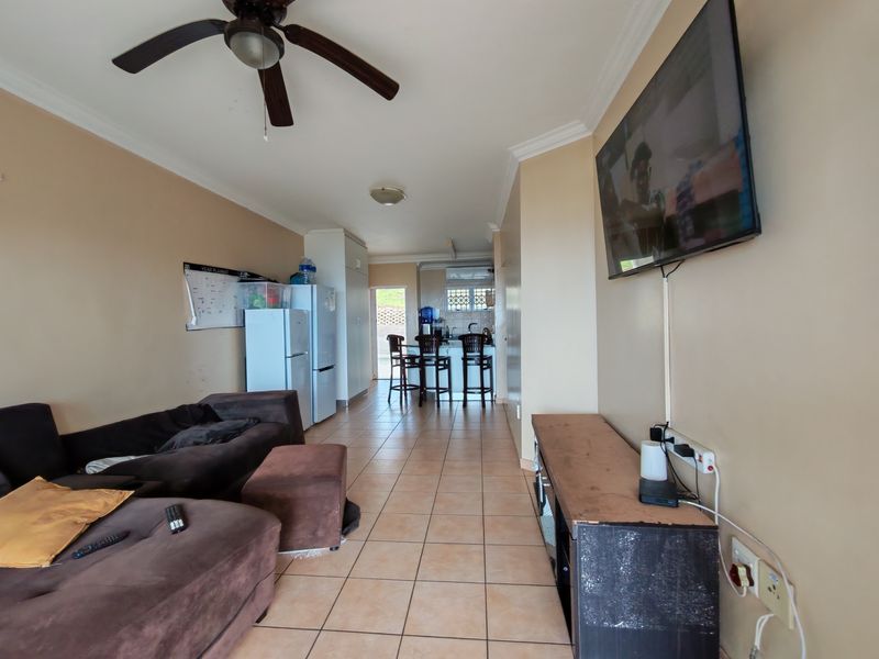 Open-plan living and kitchen area featuring ceramic floor tiles, ceiling fan, and functional kitchen cabinetry with a breakfast bar layout.