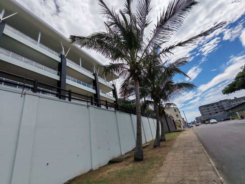 Street-level view of the apartment complex exterior, featuring a perimeter wall with electric fencing and multi-level balconies.