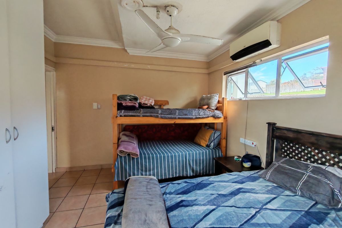 A functional bedroom featuring tiled flooring, a ceiling fan, a wall-mounted air conditioner, and built-in wardrobe storage.