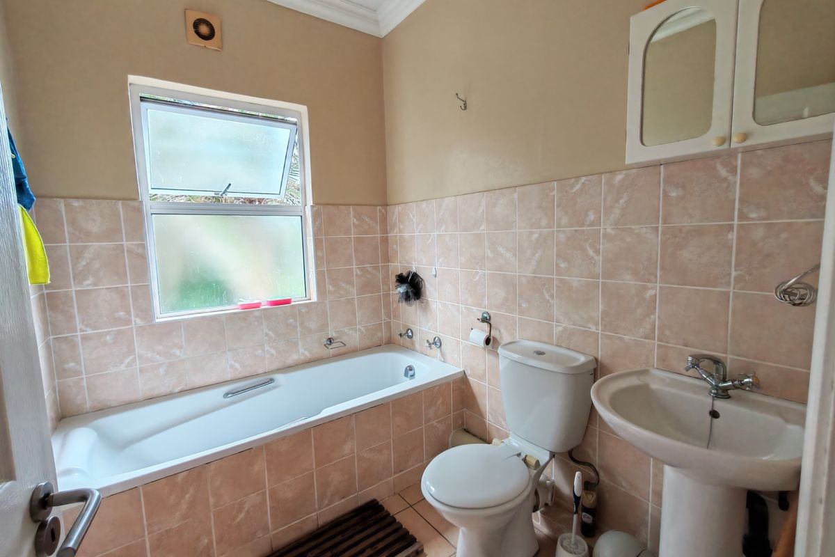 A functional bathroom featuring a bathtub, pedestal basin, and toilet, finished with neutral wall tiles and a top-hung window for ventilation.