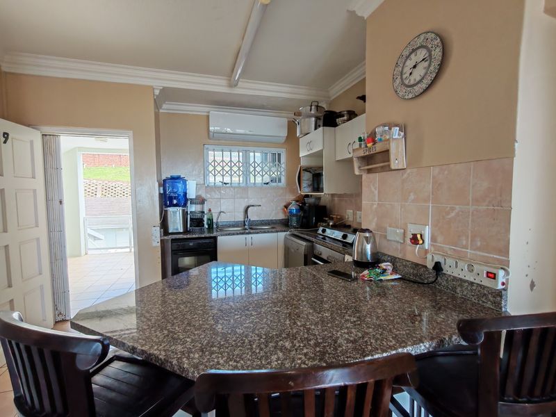 A functional kitchen featuring granite countertops, built-in cabinetry, and a tiled backsplash, with direct access to an outdoor balcony area.