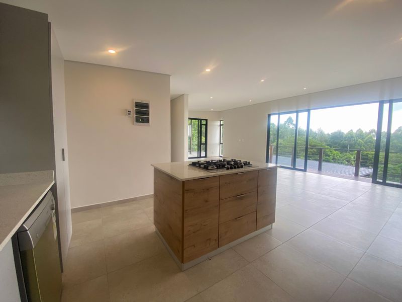 Modern open-plan kitchen featuring a central island with a built-in gas hob, sleek cabinetry, and large sliding doors opening to a scenic balcony.