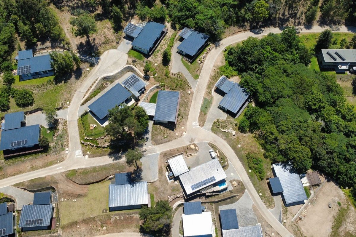 Aerial view of a cluster development featuring multiple residential units with dark metal roofing, solar panels, and integrated paved access roads within a landscaped estate.