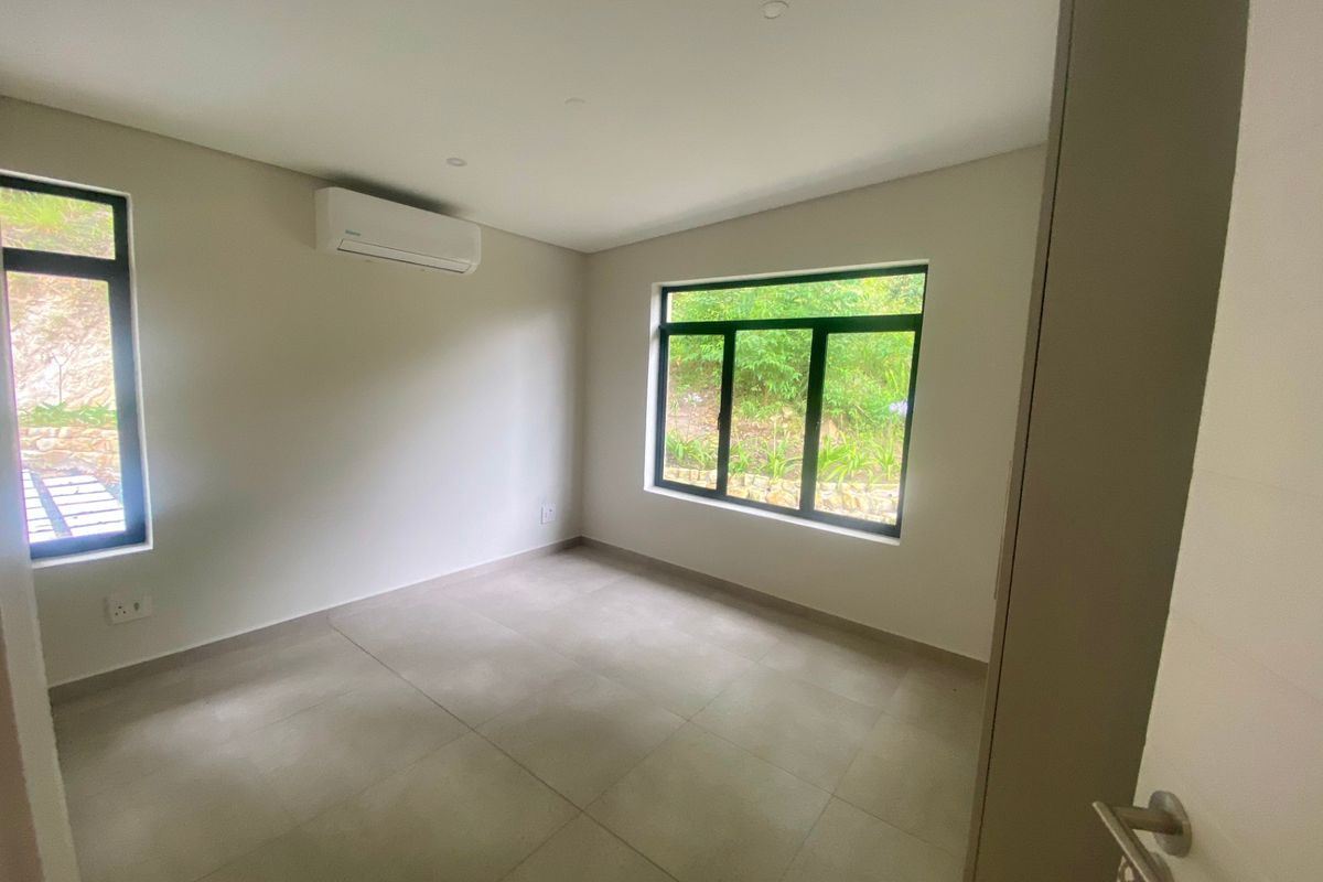 A bright, empty bedroom featuring neutral tiled flooring, modern black-framed windows, and a wall-mounted air conditioning unit.