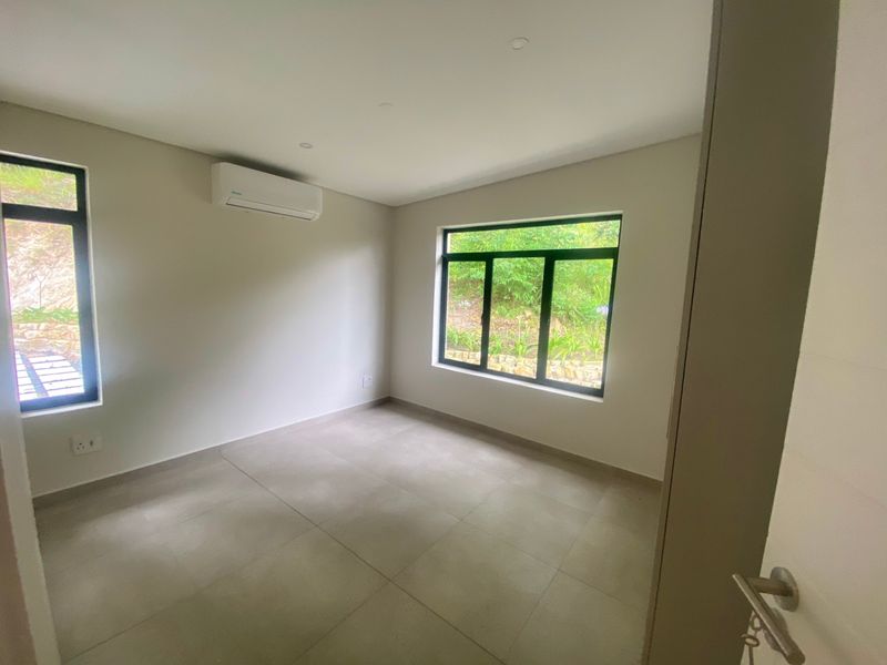 A bright, empty bedroom featuring neutral tiled flooring, modern black-framed windows, and a wall-mounted air conditioning unit.