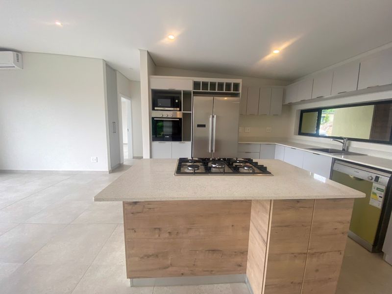 Modern open-plan kitchen featuring a central island with a gas hob, built-in oven, microwave, and sleek cabinetry with stone countertops.