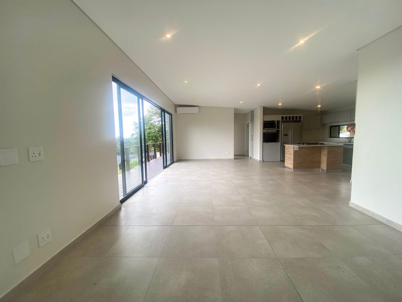 Spacious open-plan living area featuring large sliding glass doors, recessed lighting, and a modern kitchen with built-in cabinetry and appliances.