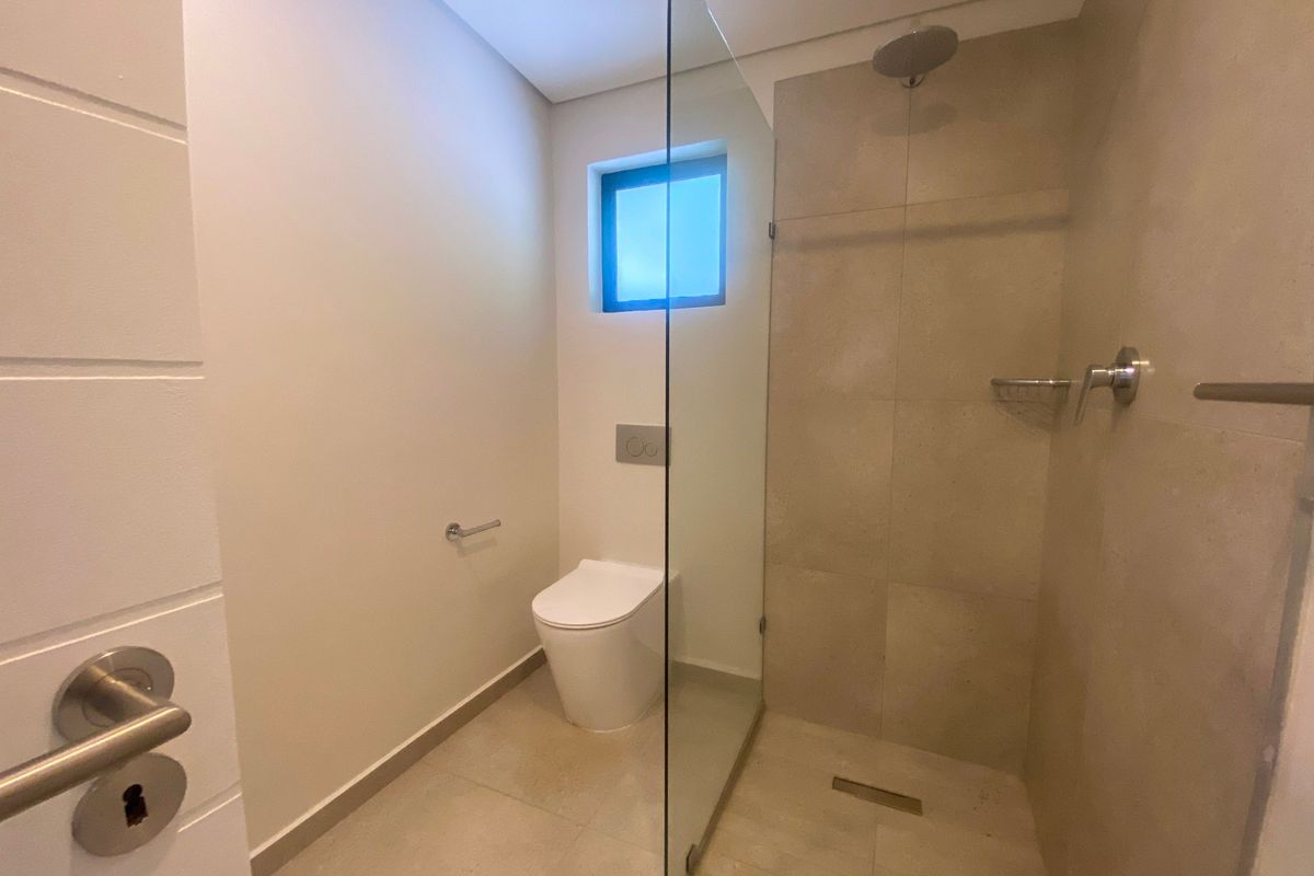 Modern bathroom featuring a walk-in shower with a glass partition, wall-mounted toilet, and neutral floor-to-ceiling tiling.