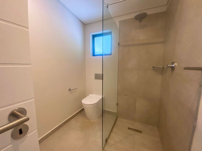 Modern bathroom featuring a walk-in shower with a glass partition, wall-mounted toilet, and neutral floor-to-ceiling tiling.
