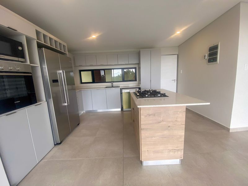 Modern kitchen featuring a central island with a gas hob, built-in oven, microwave, and sleek cabinetry with stone countertops.