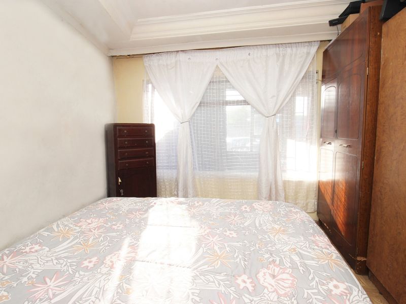 A compact bedroom featuring a built-in wooden wardrobe and coved ceiling detail, offering a functional space with potential for cosmetic updates.