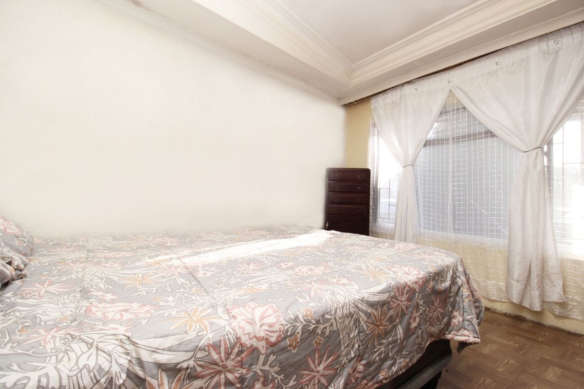 A bedroom featuring parquet flooring and coved ceilings, with visible signs of wear including ceiling staining and paint damage near the window.