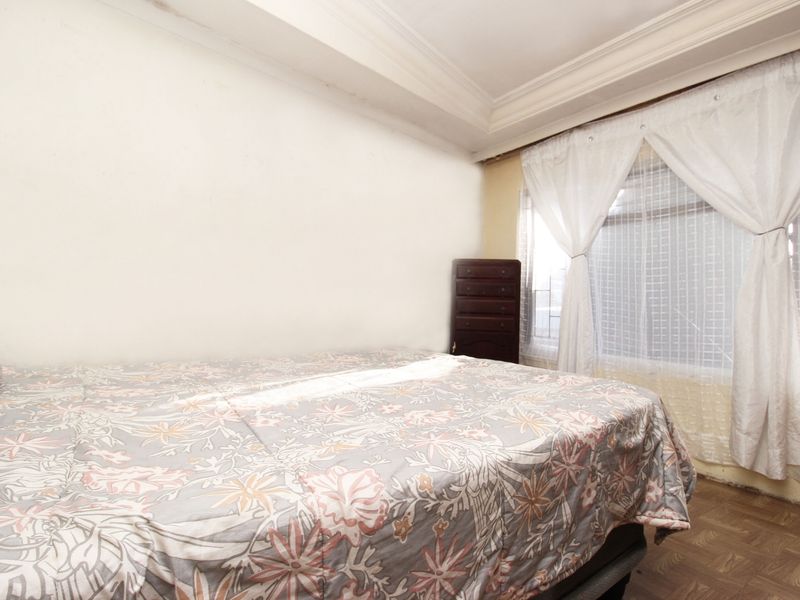 A bedroom featuring parquet flooring and coved ceilings, with visible signs of wear including ceiling staining and paint damage near the window.