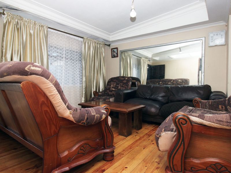 A living room featuring timber flooring, a large wall-mounted mirror, and coved ceiling cornicing, offering a dated interior space ready for modernization.