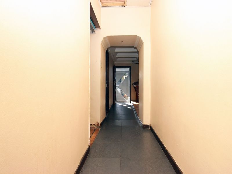 A narrow interior hallway featuring tiled flooring and an arched transition, leading towards an exterior security gate.