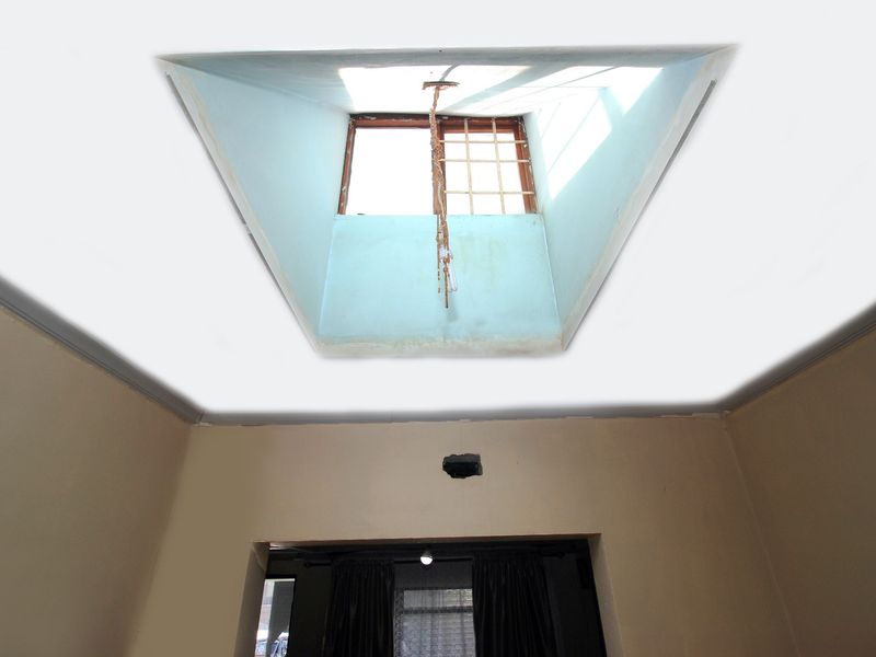 An interior view of a room featuring a skylight with visible damage to the frame and surrounding ceiling, and a hole in the wall.
