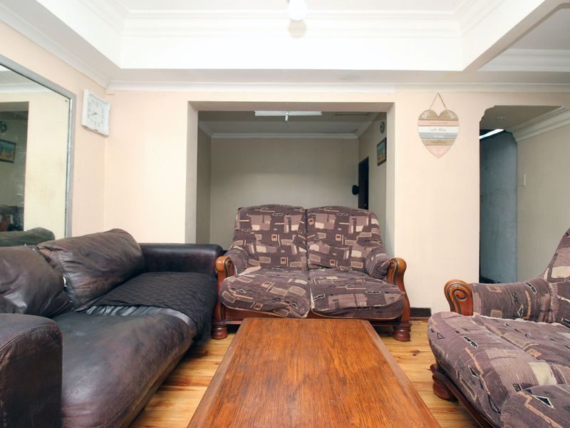 A living room featuring timber flooring, coved ceilings, and a recessed wall alcove, offering a functional space with potential for cosmetic updates.