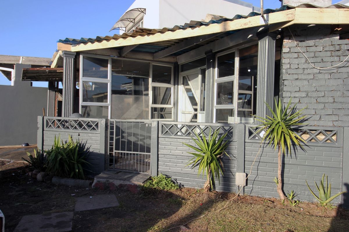 Rear exterior view of the property featuring a painted brick facade, corrugated roofing, and a small enclosed patio area with security gate.