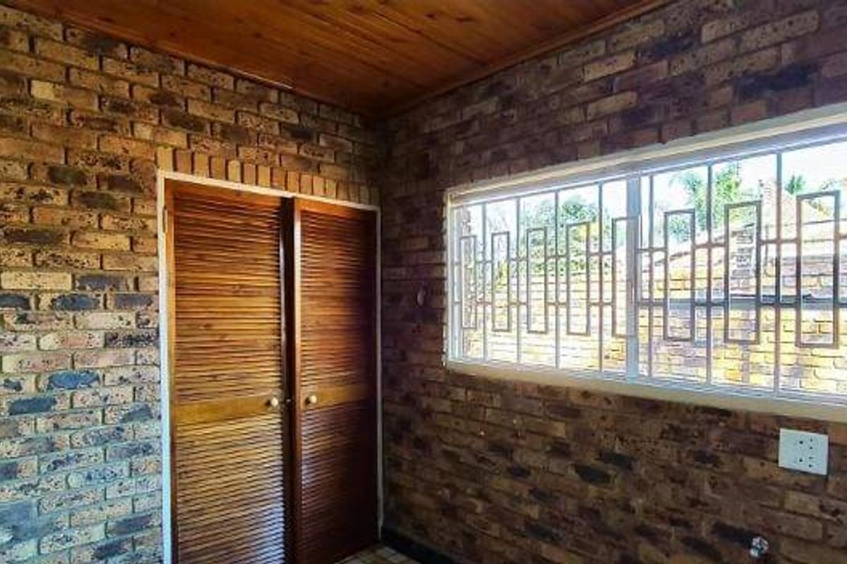 A bedroom featuring exposed brick walls, a timber ceiling, and built-in louvered closet doors, providing a rustic aesthetic.