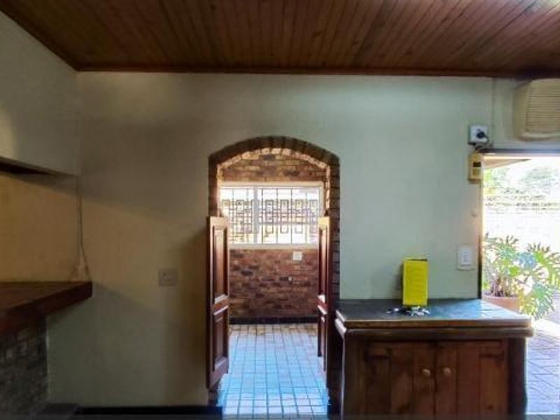 A dated kitchen area featuring brick wall accents, timber ceiling, and tiled flooring, offering a functional layout with direct access to the exterior.