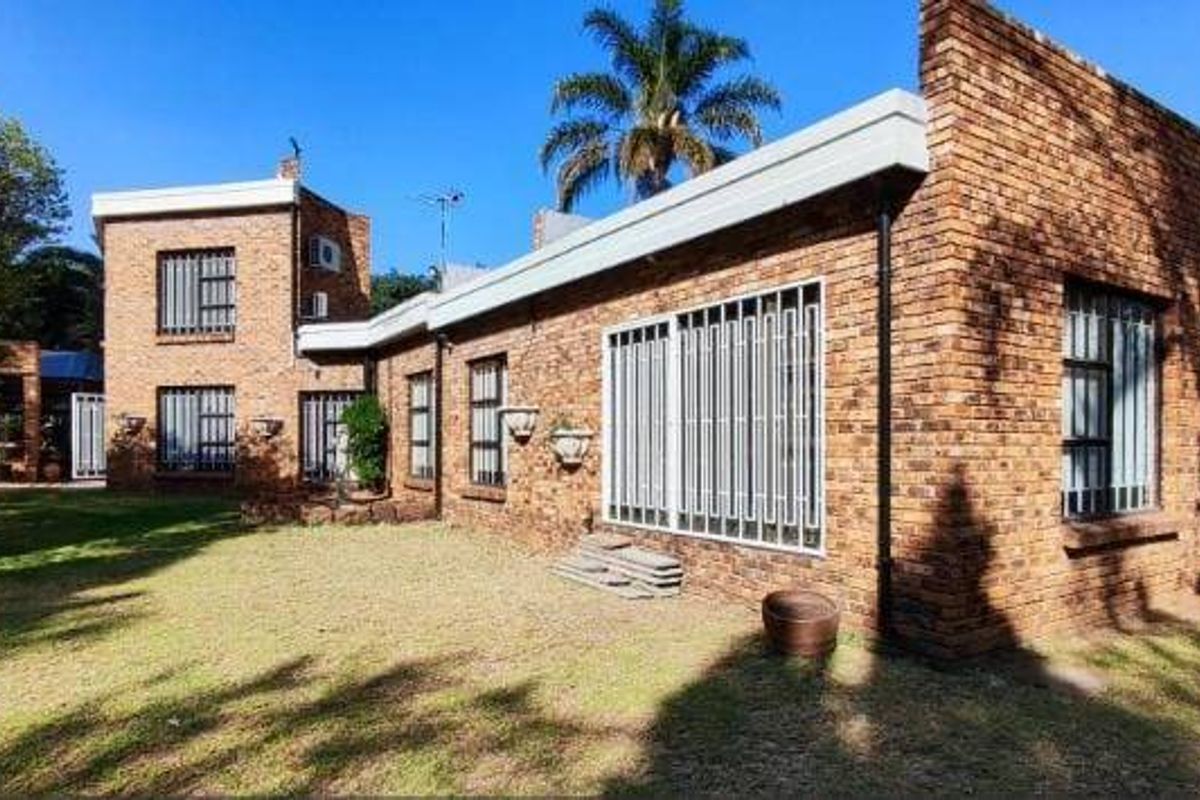 Rear view of a face brick house featuring a spacious lawn, security bars on windows, and an outdoor entertainment area with a built-in braai.