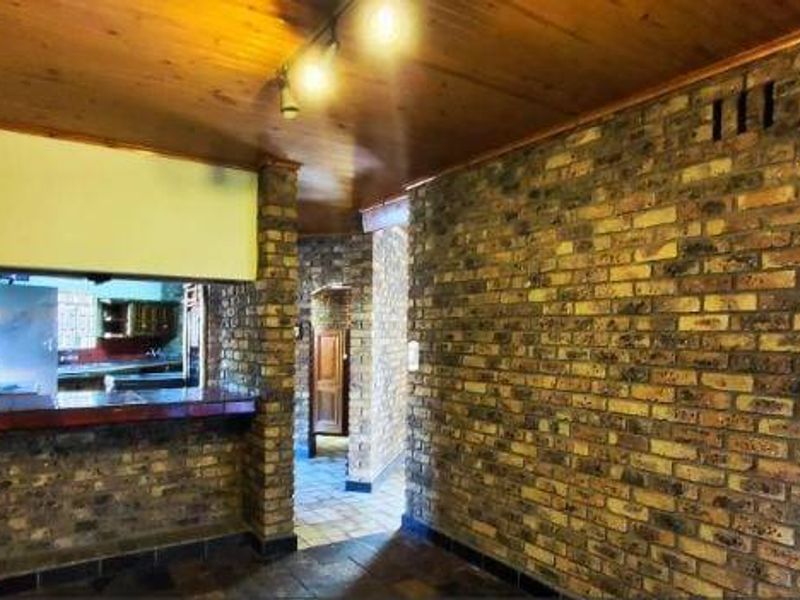 Open plan living area featuring exposed brick walls, timber ceiling, and a breakfast bar overlooking the kitchen space.