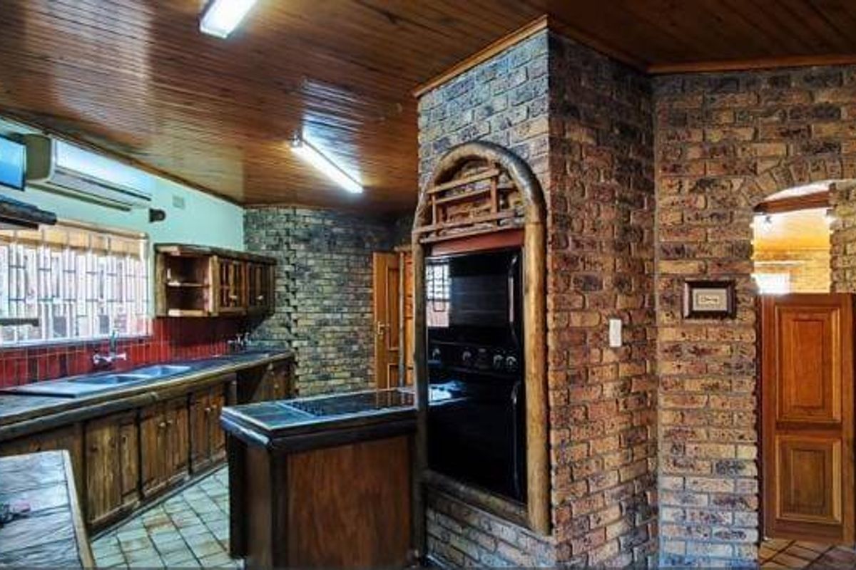 A rustic kitchen featuring exposed brick walls, timber ceiling, built-in oven, and wooden cabinetry, offering a traditional aesthetic with potential for modernization.