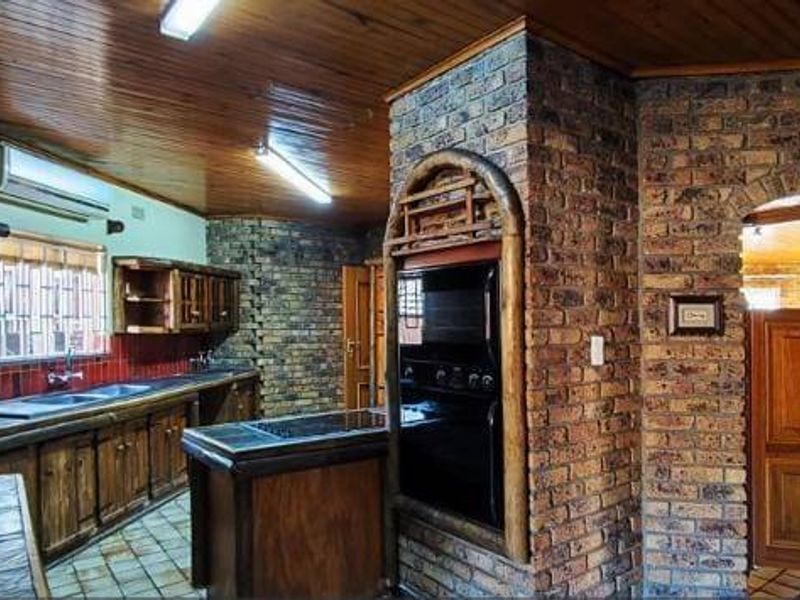 A rustic kitchen featuring exposed brick walls, timber ceiling, built-in oven, and wooden cabinetry, offering a traditional aesthetic with potential for modernization.