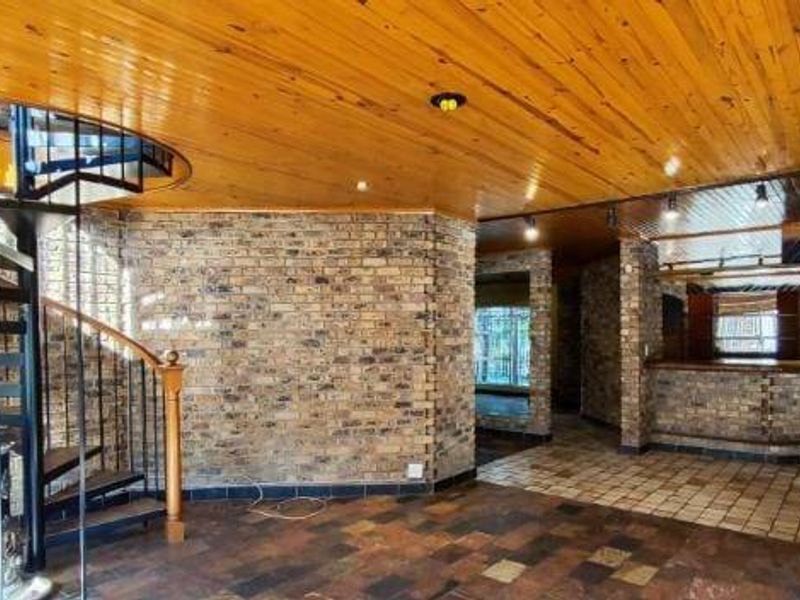 Spacious living area featuring a distinctive spiral staircase, exposed brick walls, timber ceiling, and a built-in bar counter, offering a unique architectural layout.
