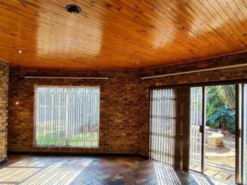 Spacious living area featuring exposed brick walls, a warm timber ceiling, slate flooring, and direct access to the garden through sliding glass doors.