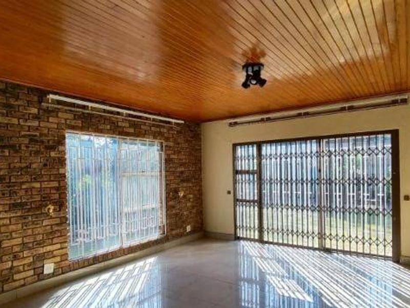 Spacious living area featuring a warm timber ceiling, exposed brick feature wall, tiled floors, and large sliding doors with security gates leading outdoors.