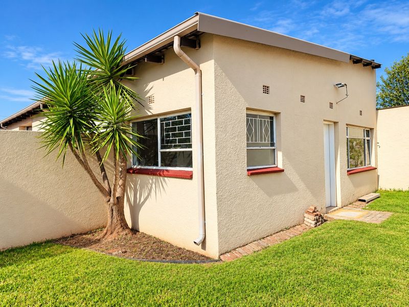 A view of the rear exterior of the apartment, featuring plastered walls, security bars on windows, and a small paved area adjacent to the lawn.