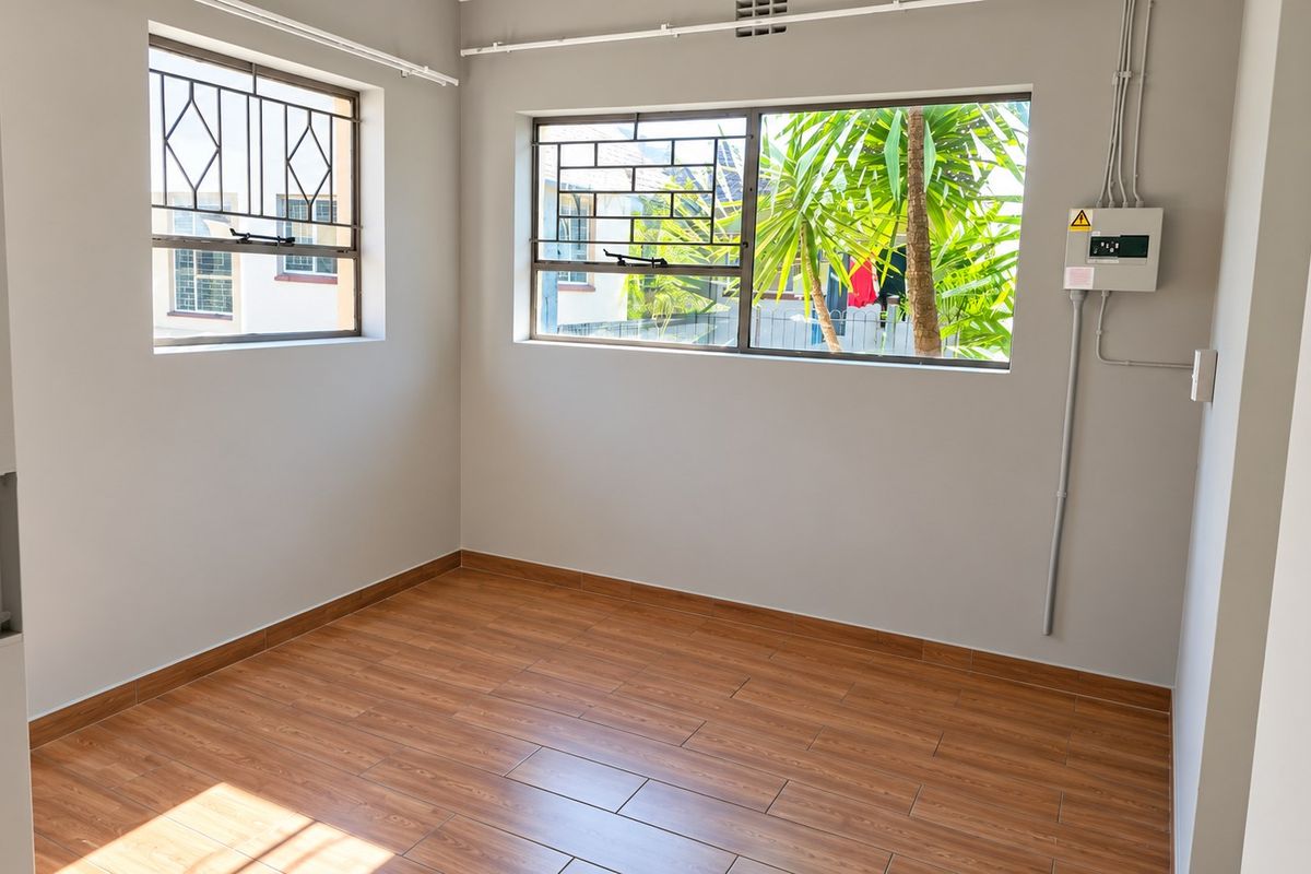 A bright, empty bedroom featuring wood-look tile flooring, neutral walls, and secure windows with fitted burglar bars.