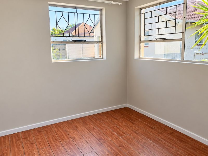 A bright, empty bedroom featuring wood-look tile flooring, neutral walls, and windows fitted with security bars.