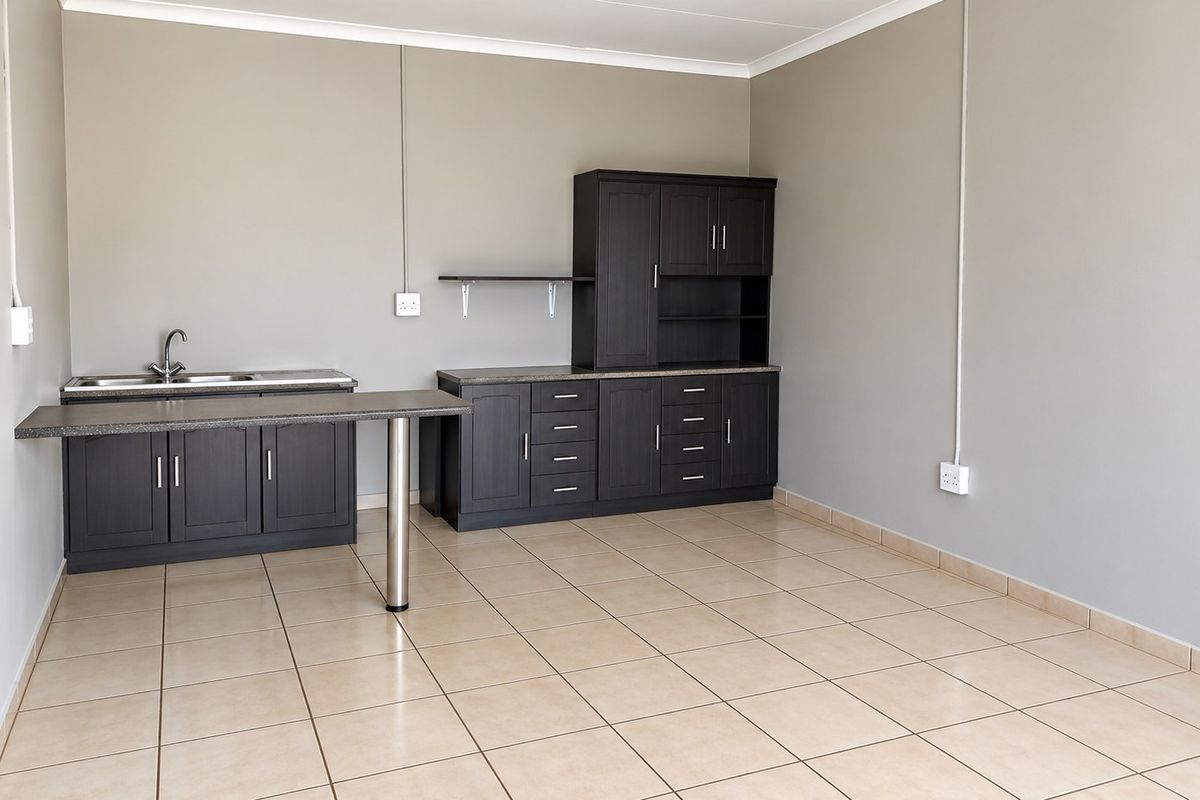 A clean, empty kitchen area featuring dark wood-look built-in cabinetry, laminate countertops, a stainless steel sink, and neutral tiled flooring.