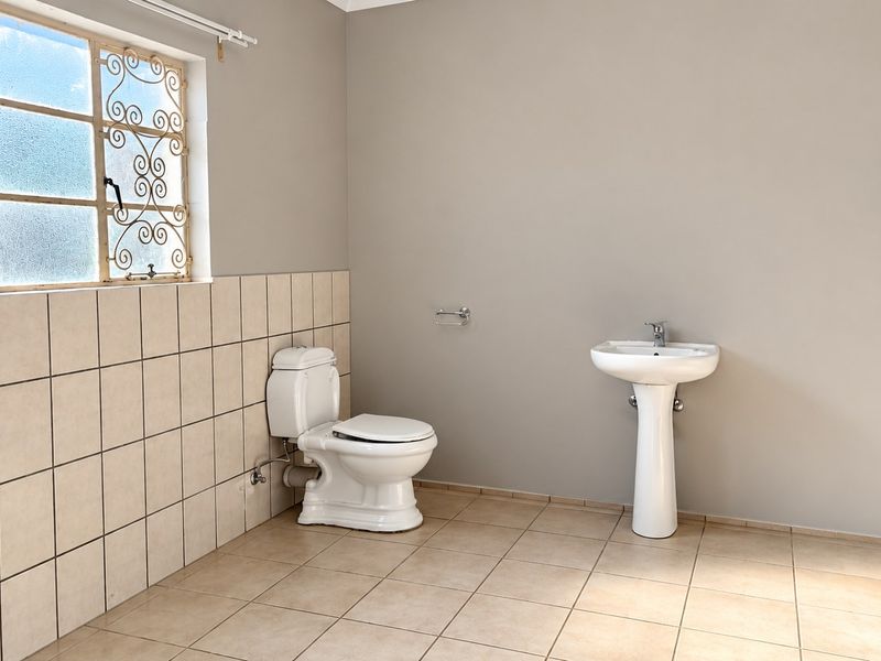 A clean, empty bathroom featuring a pedestal basin, toilet, and tiled finishes, ready for modern updates.