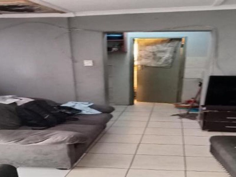 A living room area featuring tiled flooring and coved ceilings, currently showing signs of wall cracking and exposed electrical wiring.