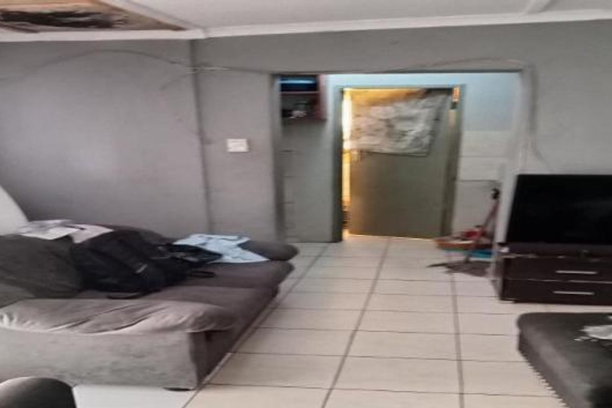 A living room area featuring tiled flooring and coved ceilings, currently showing signs of wall cracking and exposed electrical wiring.