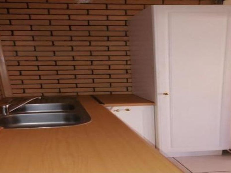 A functional scullery area featuring a stainless steel sink, laminate countertop, and exposed brick wall finish.