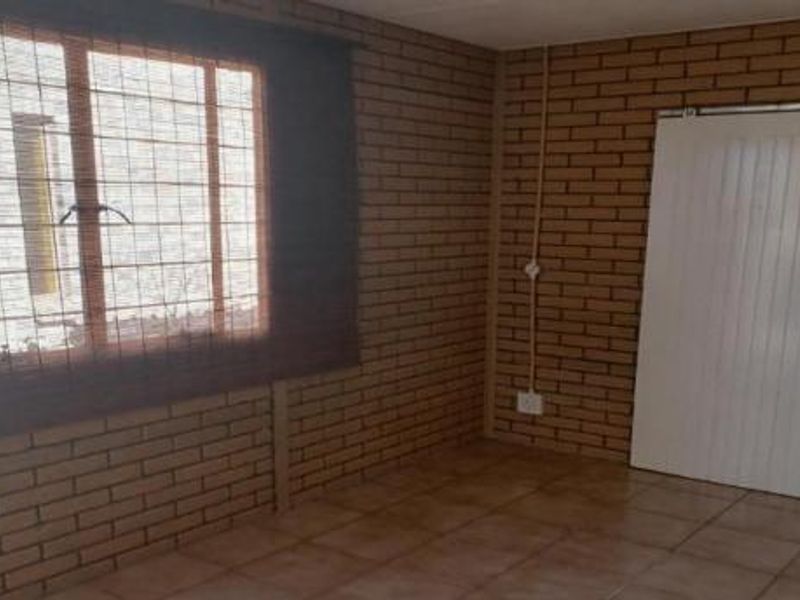 An empty living area featuring exposed brick walls, ceramic floor tiles, and a sliding door leading to an adjacent space.