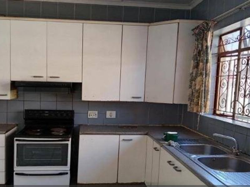 A functional kitchen featuring white built-in cabinetry, an electric stove with extractor fan, and a double basin sink with tiled backsplash.