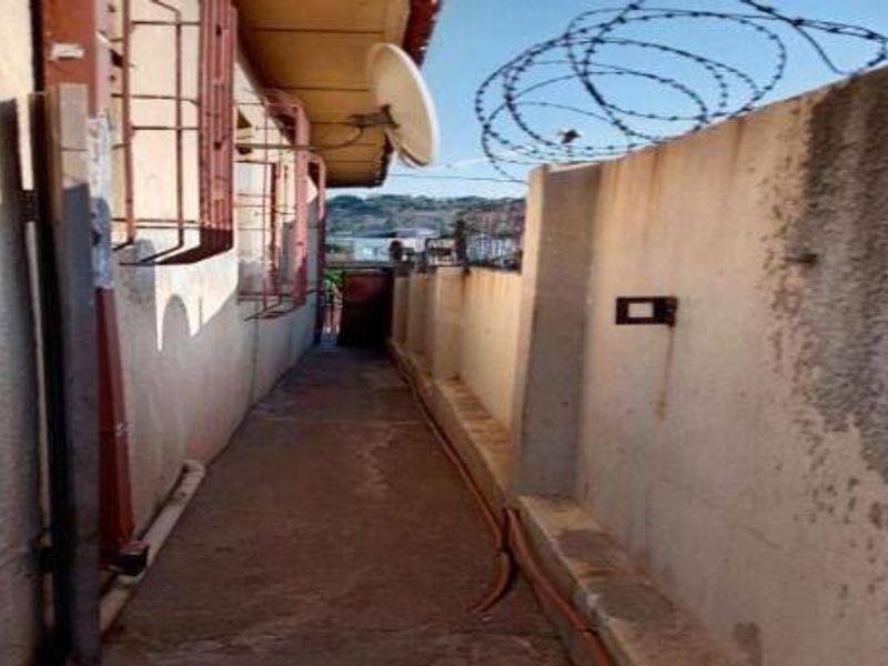 A narrow exterior side passage featuring a concrete walkway, security bars on windows, and a boundary wall topped with razor wire.