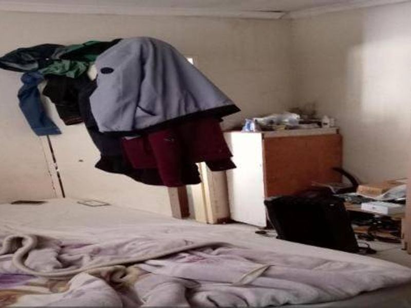 A bedroom featuring tiled flooring and a built-in wardrobe, currently showing signs of wear including peeling paint on the walls.