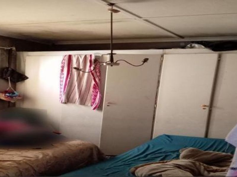 A bedroom featuring built-in cupboards and a central light fixture, showing signs of wear on the ceiling.