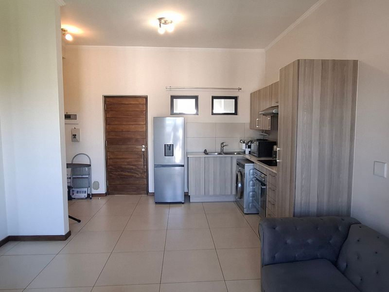 Open-plan living area featuring tiled floors and a compact kitchen with built-in cabinetry, oven, and extractor fan.